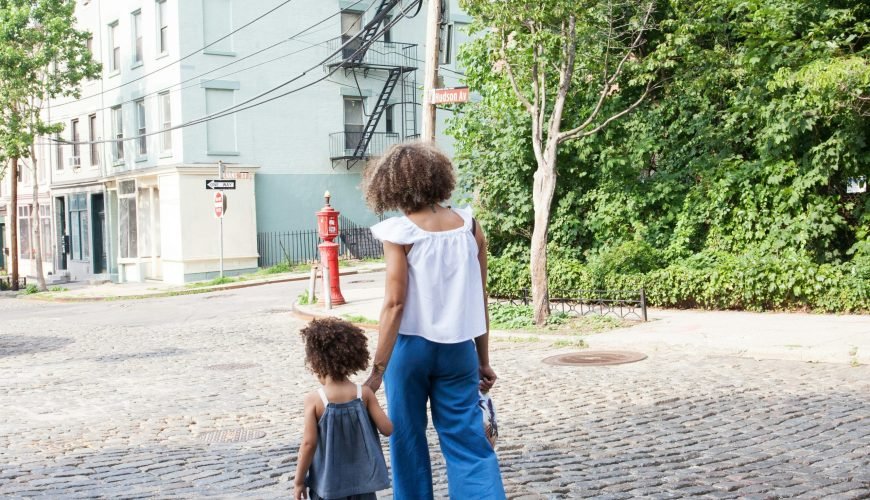 woman in white cap-sleeved shirt and blue pants walking beside girl in gray tank top