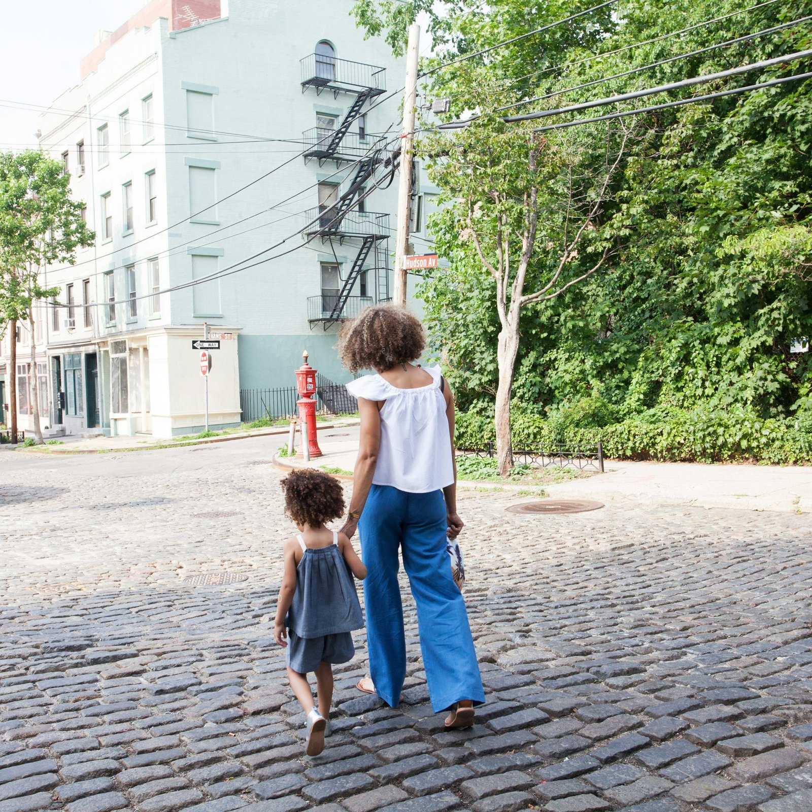 woman in white cap-sleeved shirt and blue pants walking beside girl in gray tank top